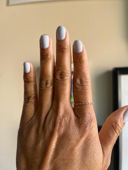 Hand with light gray nail polish and a gold ring on a neutral background